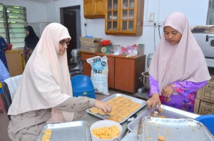 ASFAH Mohd. Shariff (kiri sekali) mengeluarkan kuih daripada acuan sambil dibantu salah sseorang pekerja.