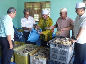 ABDUL Hadi Edar memasukkan bungkusan ikan kering yang dibeli ADUN Sungai Bakap, Maktar Shapee (tengah) sambil diperhatikan Pegawai Penyelaras KADUN Sungai Acheh, Mohd. Kamil Abu Bakar (kanan sekali).
