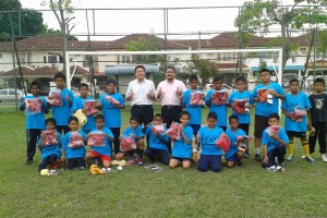 SIM Tze Tzin (berdiri, lima dari kiri) dan Mohamad Shawal Ahmed (berdiri, enam dari kiri) menunjukkan tanda bagus selepas selesainya Majlis Penyampaian Sumbangan Kelengkapan Pakaian Sukan di Padang Bola Sepak Taman Sri Nibong di sini baru-baru ini.