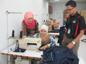 SARIFAH Mohd. Idris (paling kiri) sedang memberi tunjuk ajar kepada pelatih ibu tunggal mengenai teknik menjahit pakaian secara komersial sambil diperhatikan pegawai Zakat Pulau Pinang (paling kanan).