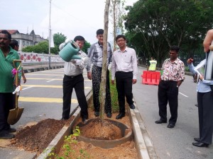 CHOW Kon Yeow (kiri sekali) menyempurnakan gimik menanam dan menyiram pokok Penaga Lilin di Jalan Datok Keramat sambil diperhatikan Ong Ah Teong (tengah) dan Teh Lai Heng.