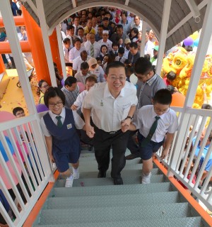 槟州首长林冠英（中）牵着学生的手，亲身使用光华学校行人天桥。