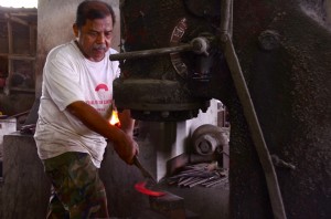 ABDULLAH Ismail menggunakan mesin mengetuk besi untuk membentuk sabit.